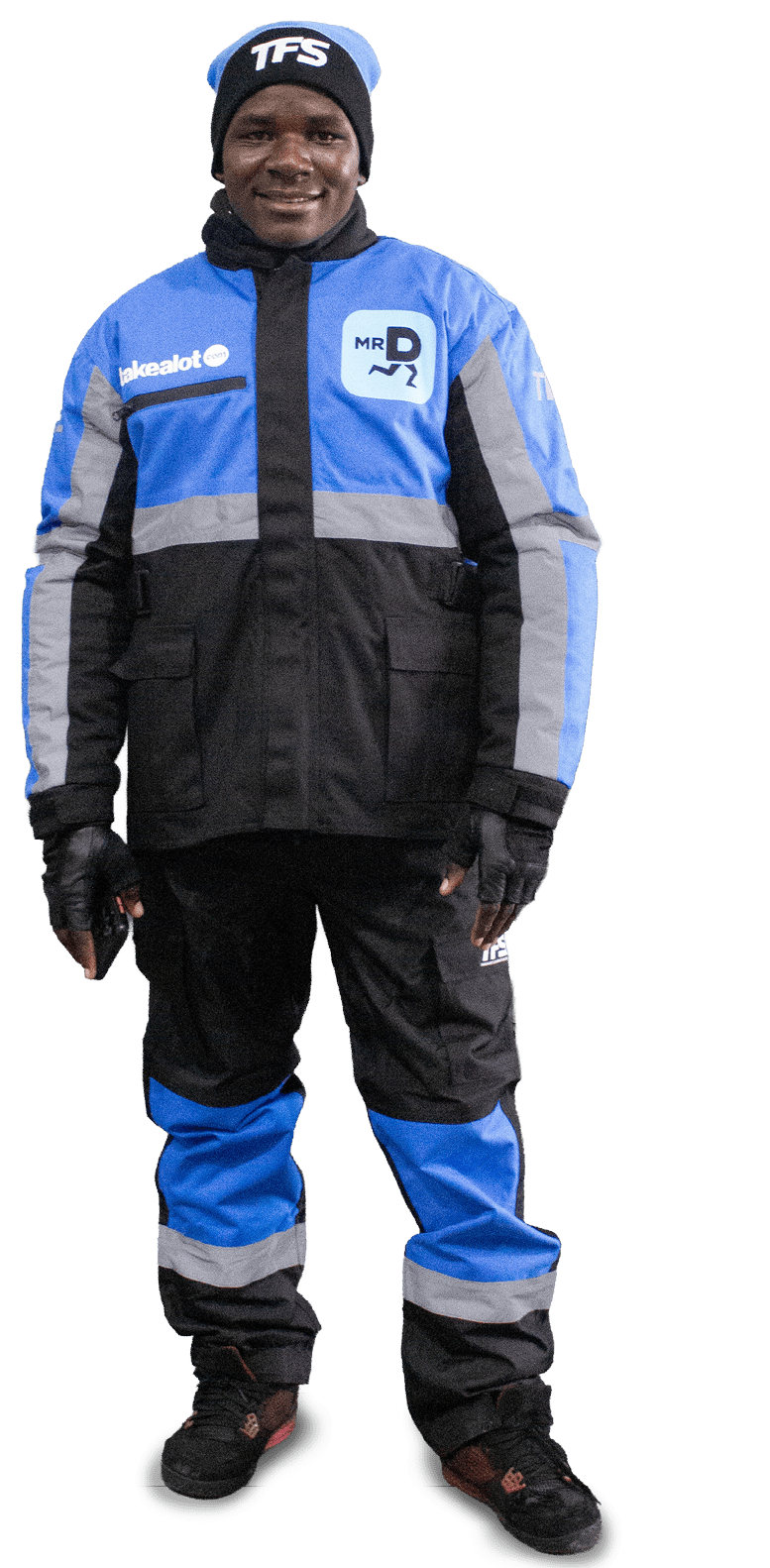 A person wearing a blue, black, and gray winter jacket and pants with gloves and a black beanie hat is standing and smiling. Description generated by AI